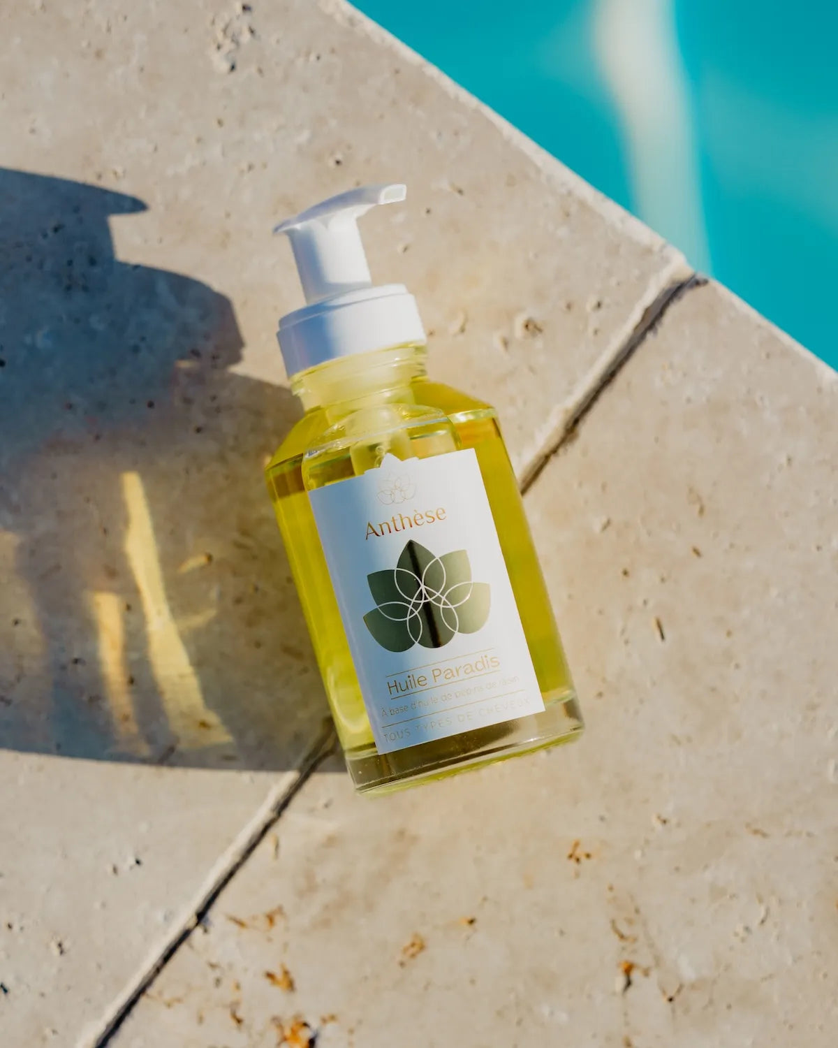 Huile Paradis Anthèse posée sur le bord d'une piscine – soin capillaire naturel.